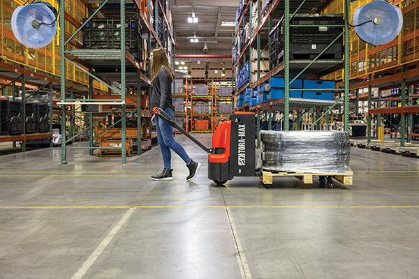 A woman operates a Tora-Max Electric Pallet Jack in a warehouse
